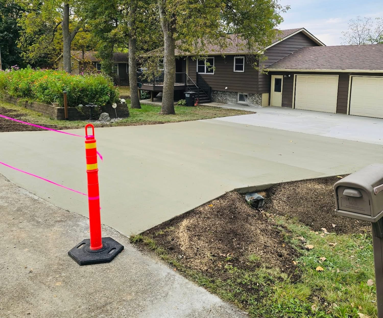 Fresh driveway pour roped off with cones at a wooded home